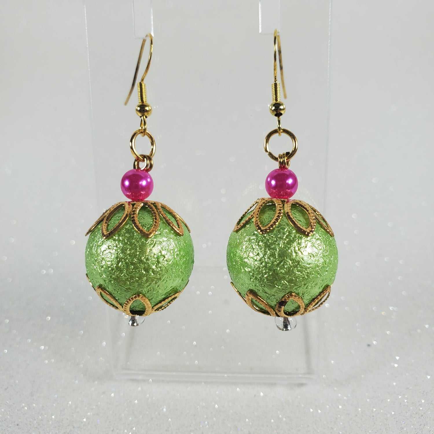Green beaded earrings with pink beads on a clear card against a white background