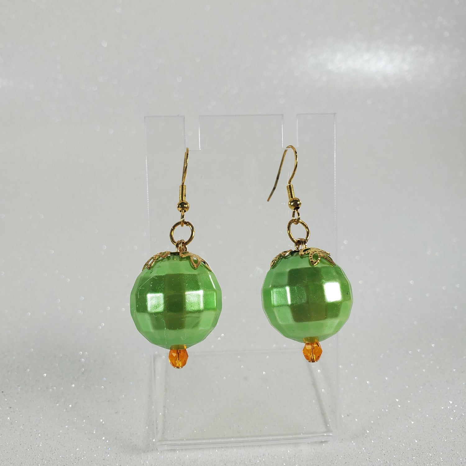 Green beaded earrings on a clear plastic stand against a light gray background