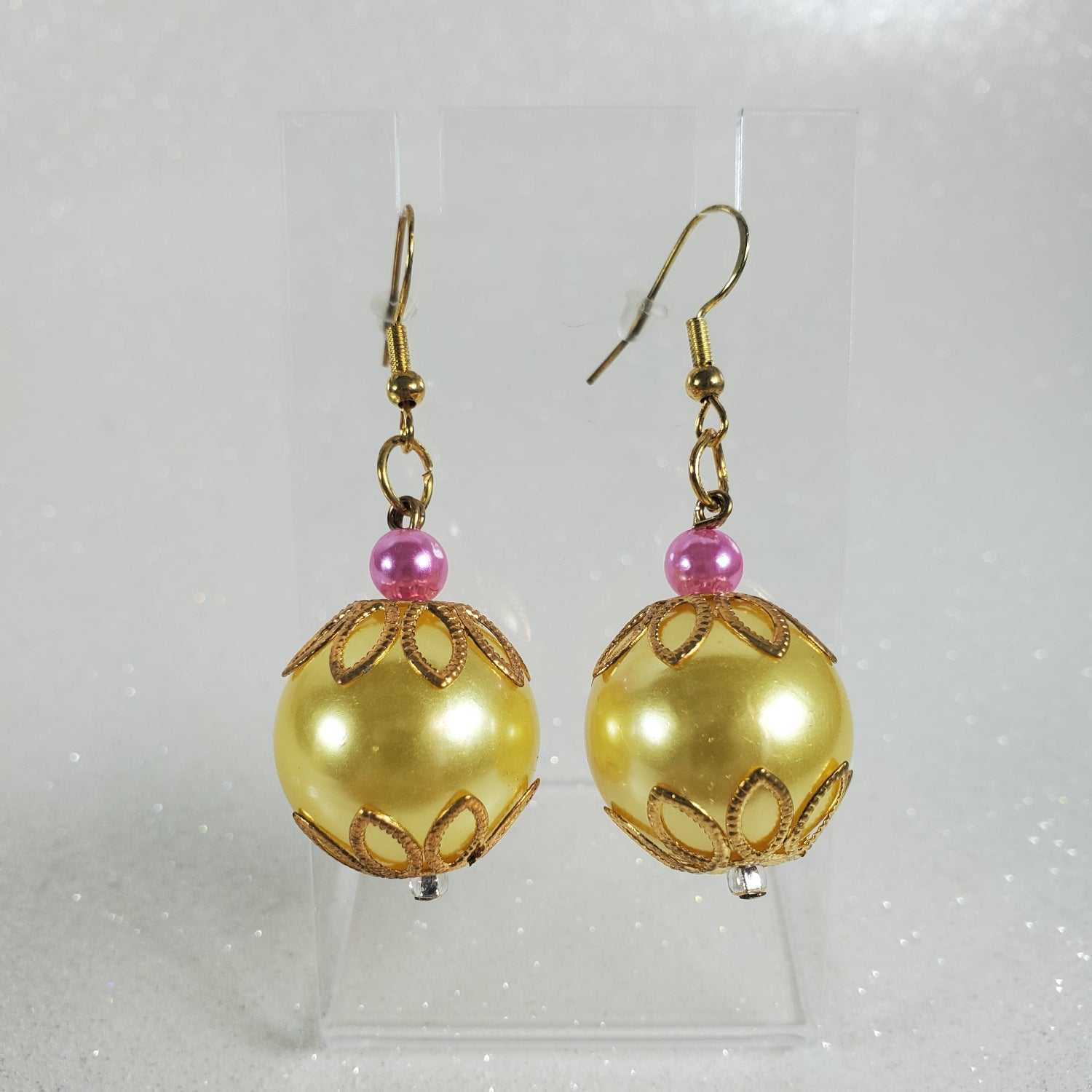 Pair of gold spherical earrings with pink beads on a clear background