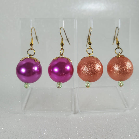 Pair of earrings with pink and gold spherical beads in a clear display case.