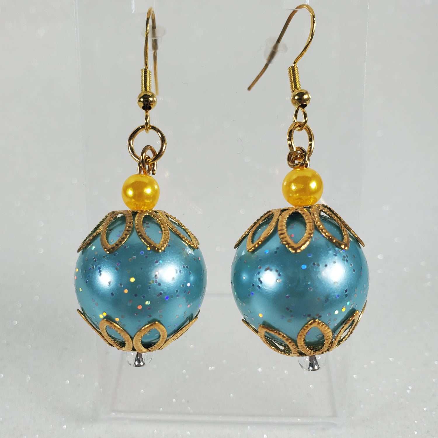 Pair of glittery blue spherical earrings with gold accents and yellow beads on a clear background