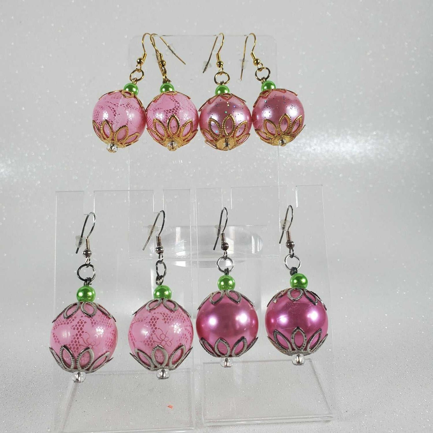 Set of pink beaded earrings with green accents on a clear stand against a white background