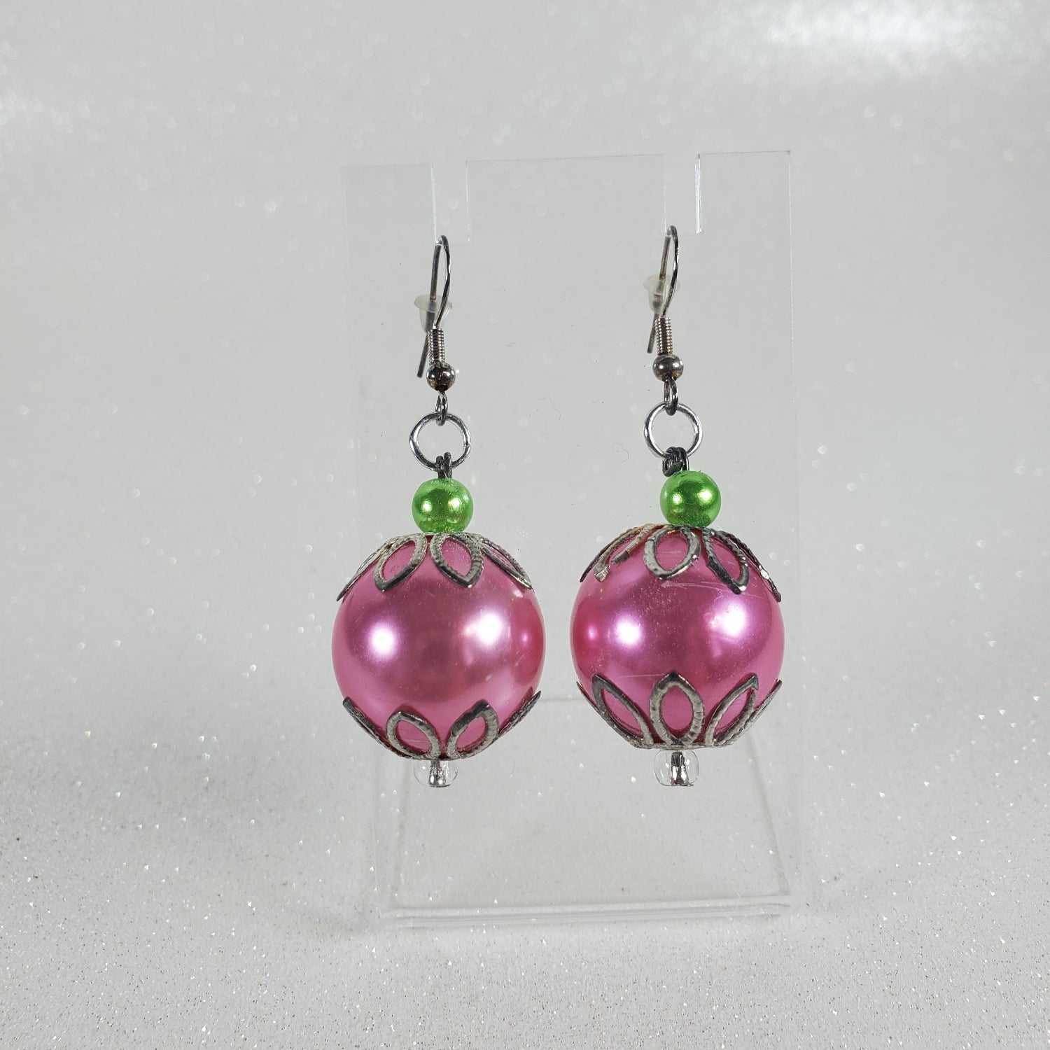 Pink beaded earrings with green accents on a clear background