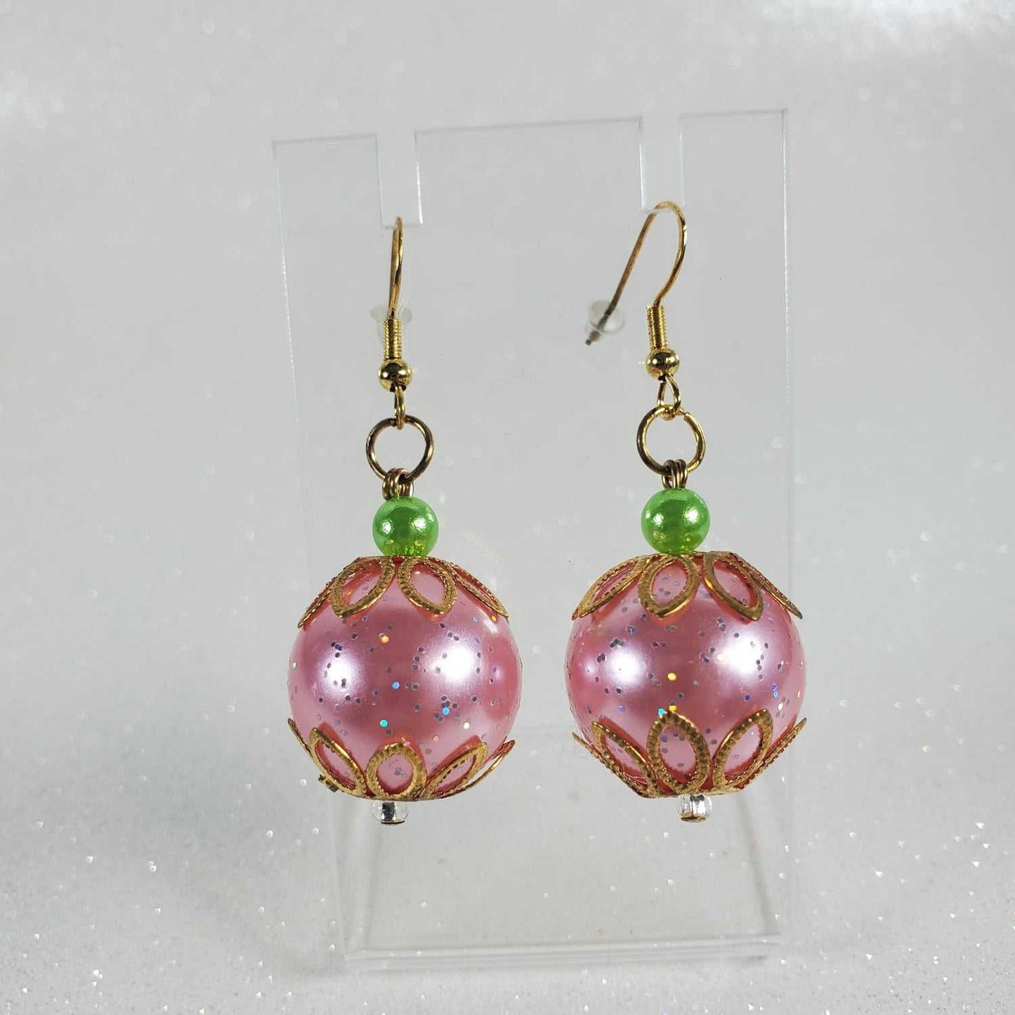 Pair of pink beaded earrings with gold accents on a clear card against a white background.