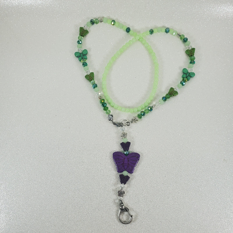 Beaded lanyard with a purple butterfly charm on a light gray background