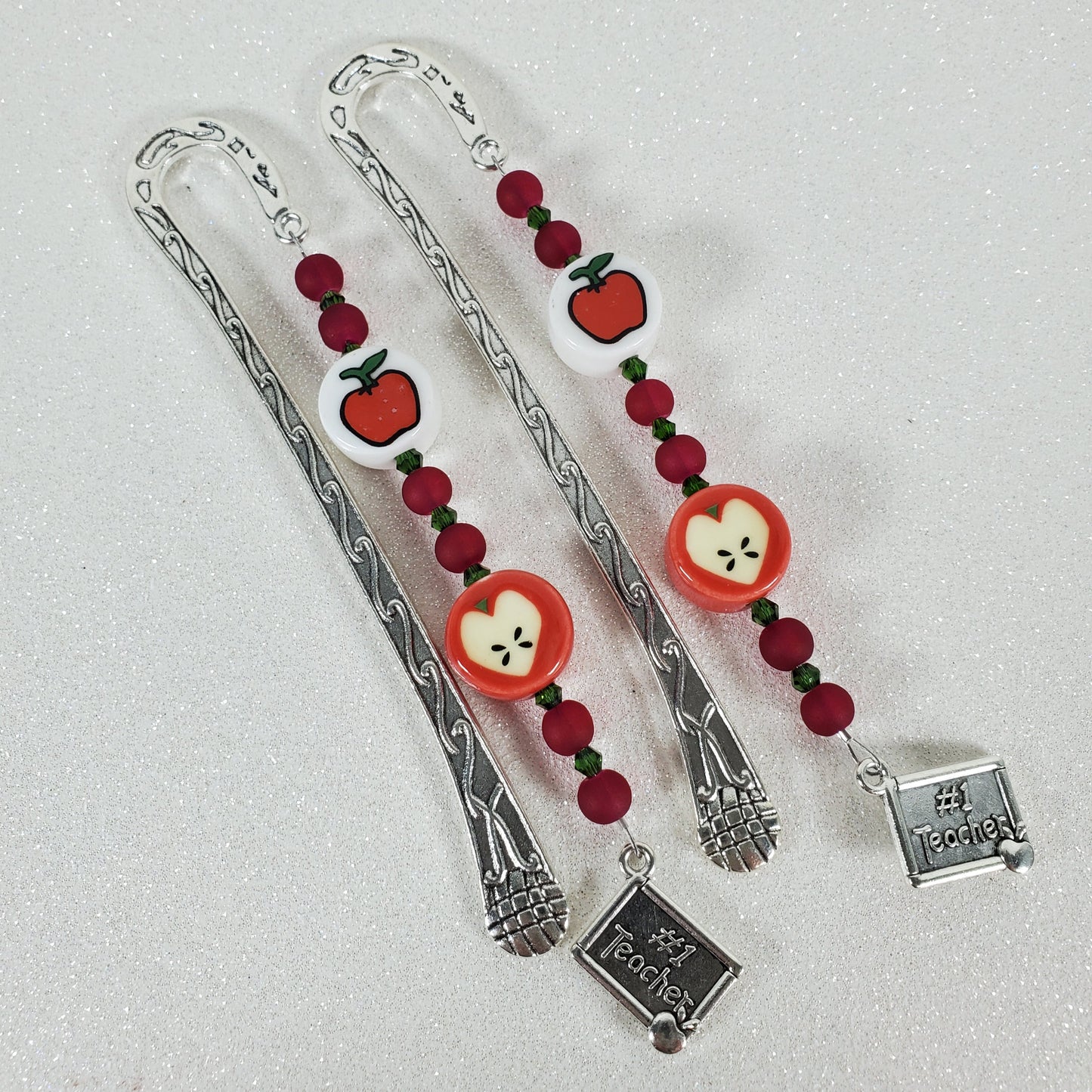 Two silver bookmarks with red apple designs on a light gray background
