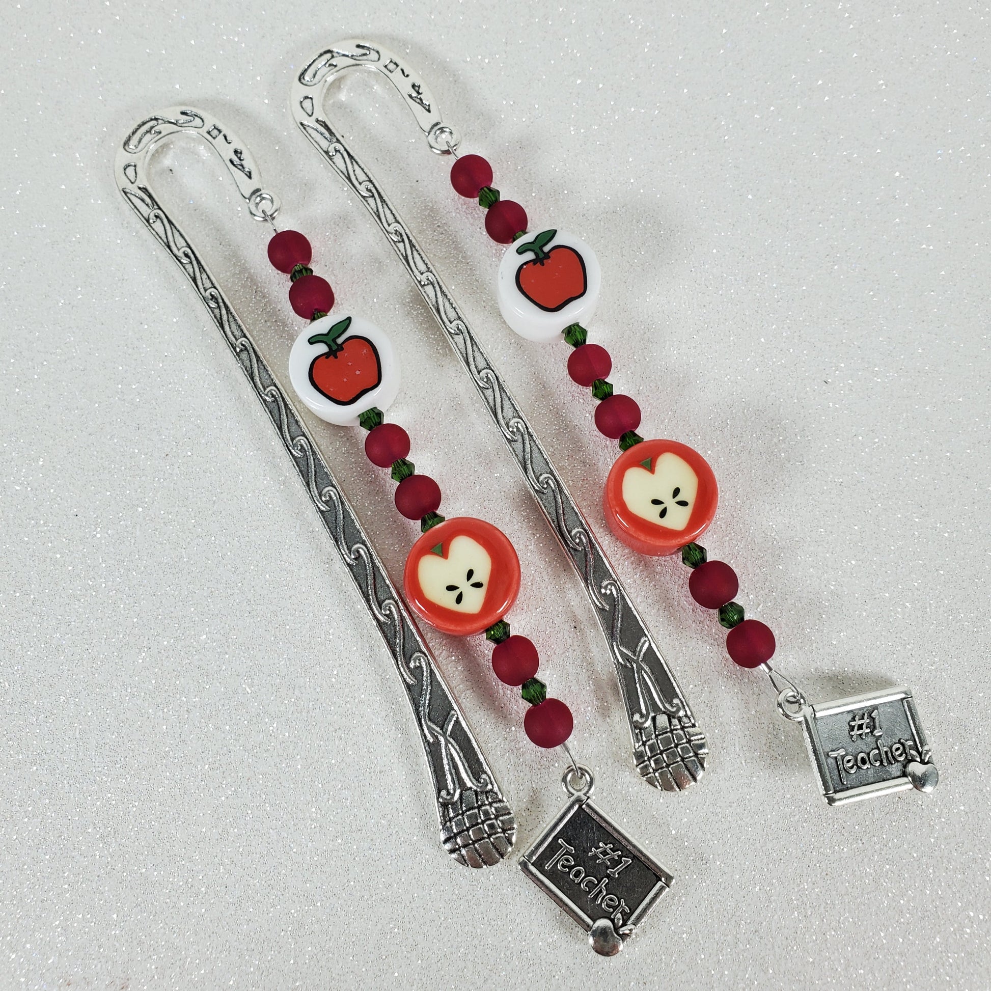Two silver bookmarks with red apple designs on a light gray background