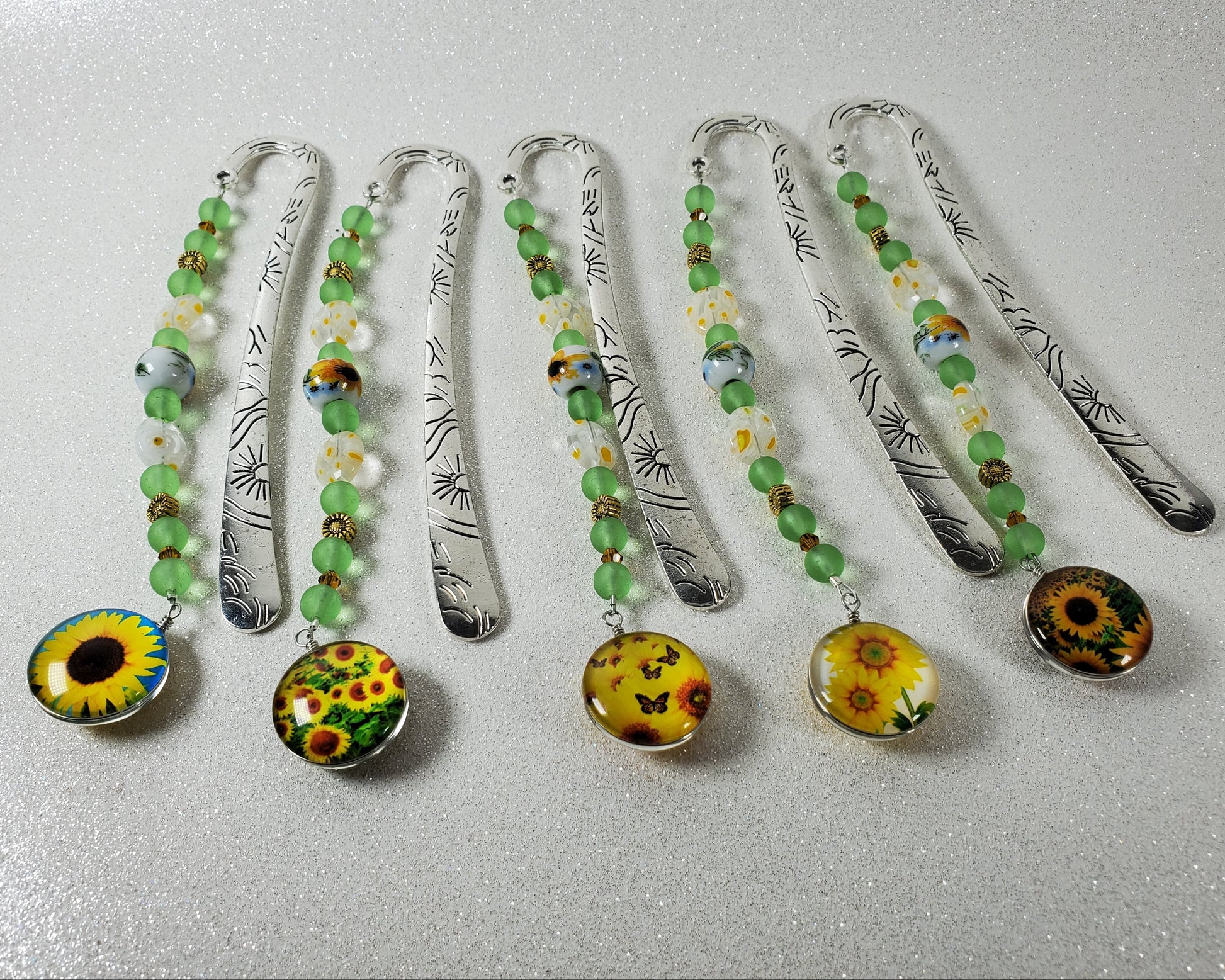 Set of five decorative bookmarks with sunflower designs on a metallic surface