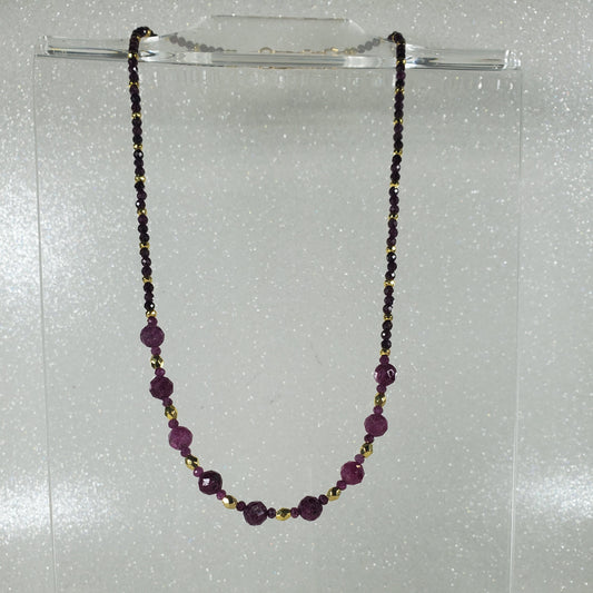 Beaded necklace with Ruby and gold beads on a clear stand against a white background