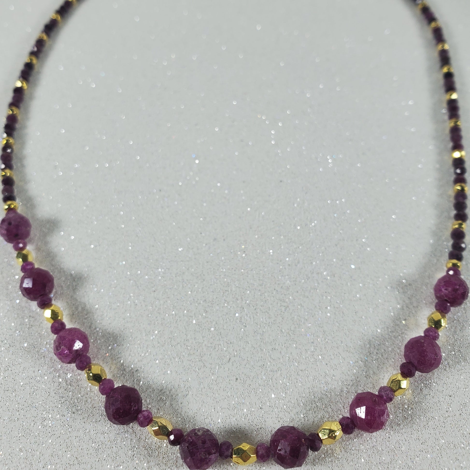 Necklace with Ruby and gold beads on a light gray background 