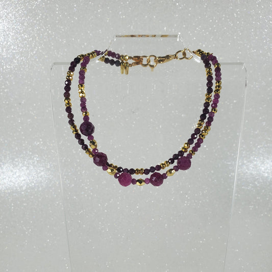 Beaded bracelet with Ruby and gold beads on a clear stand against a white background