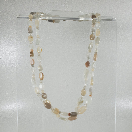 Necklace with multicolored beads on a clear stand against a light gray background