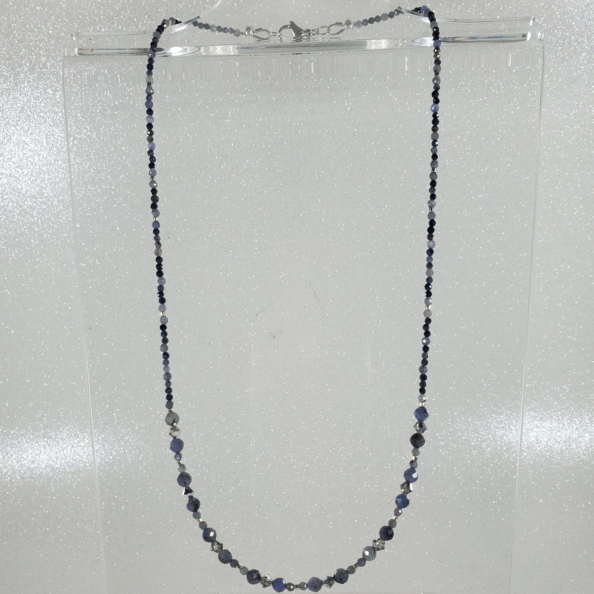 Necklace with small beads on a clear stand against a light gray background