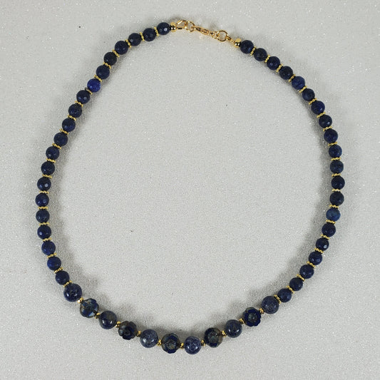 Necklace with blue beads and gold clasp on a light gray background