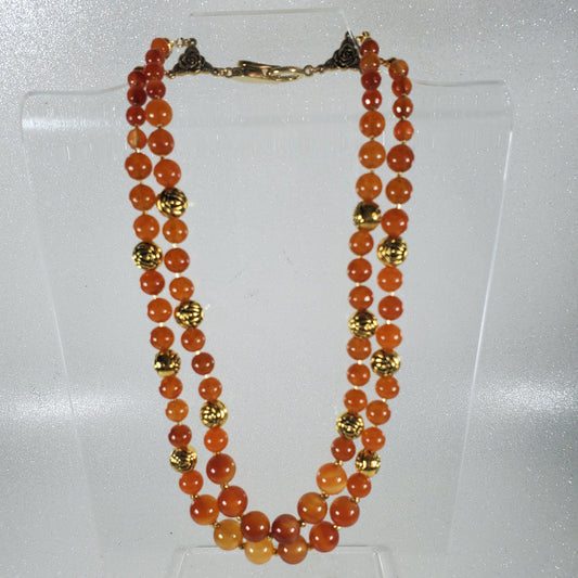 Necklace with orange beads and gold accents on a clear stand against a white background