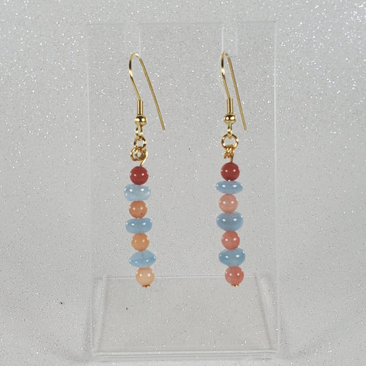 Pair of beaded earrings on a clear stand against a light gray background