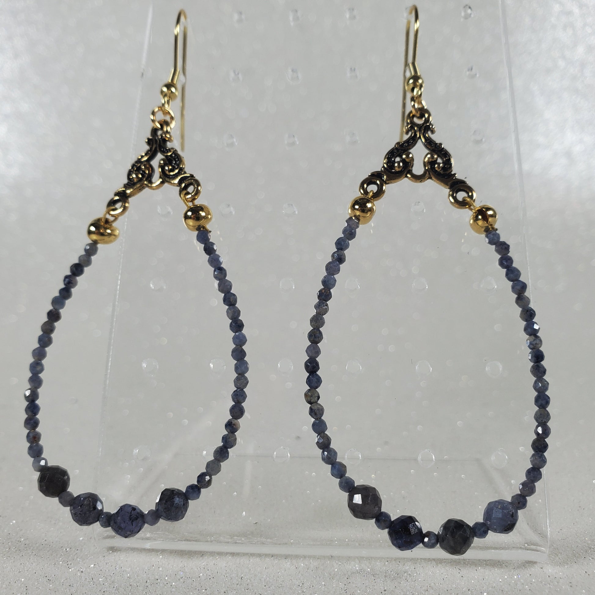 Pair of beaded earrings on a clear stand against a light gray background
