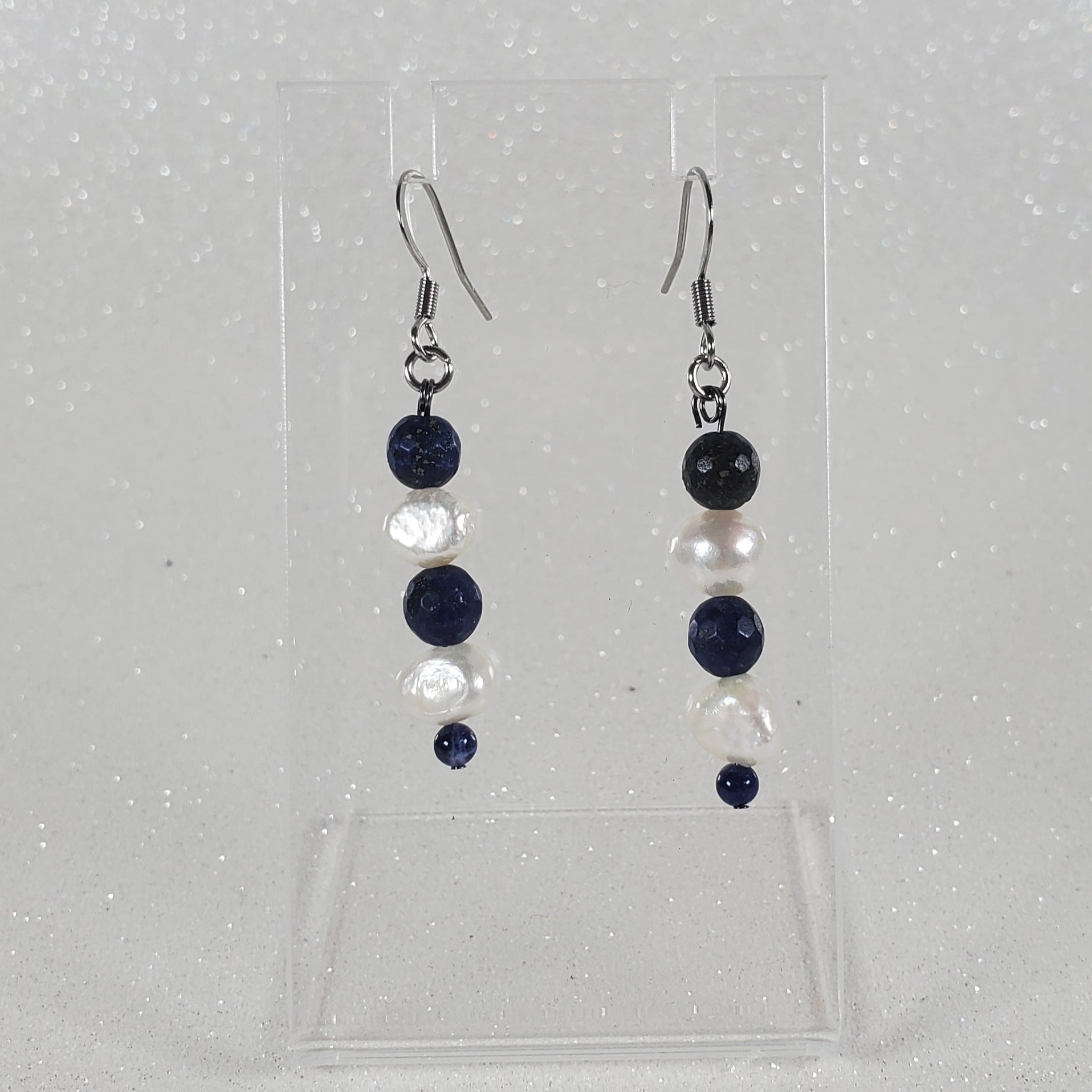 Pair of earrings on a clear plastic stand on a light gray background