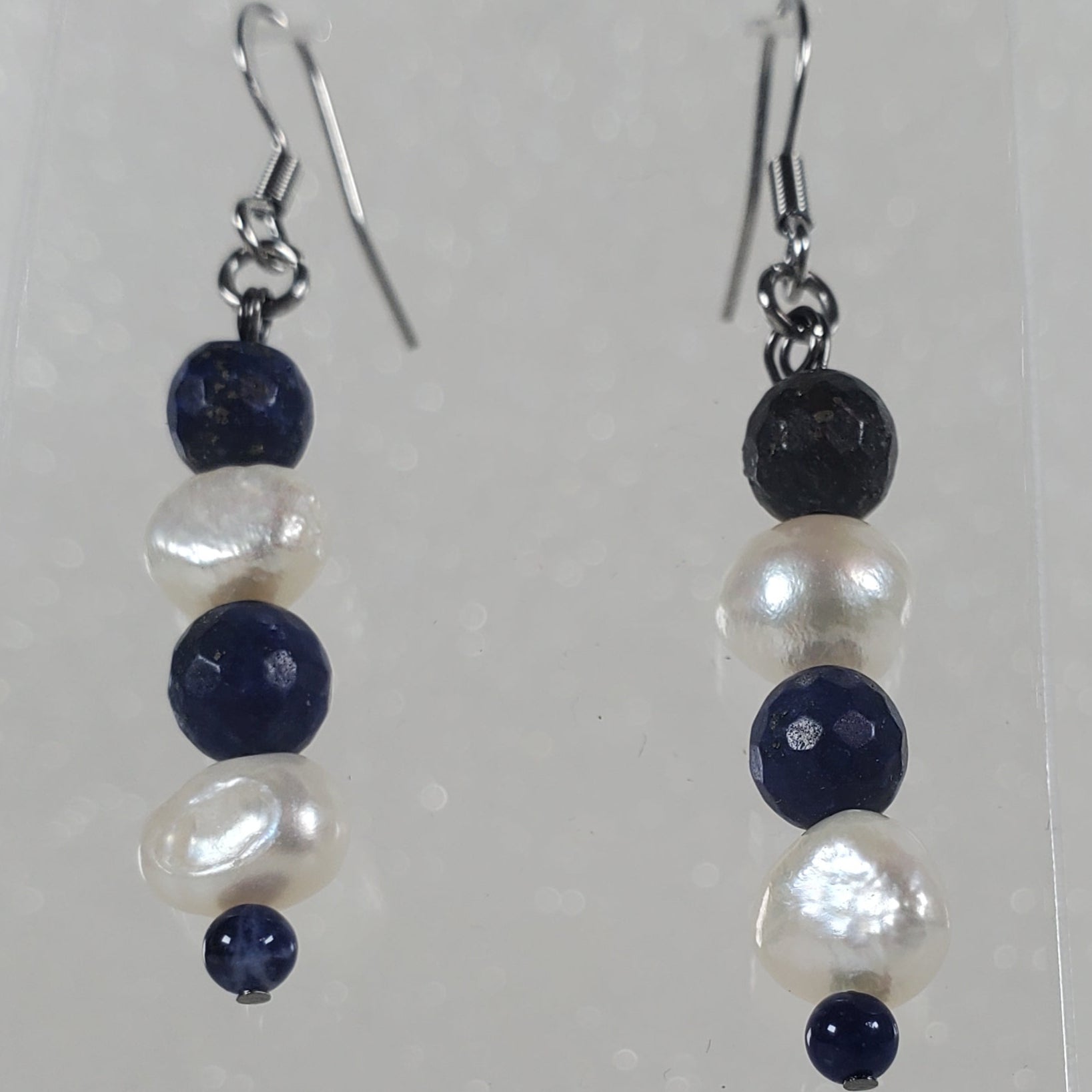 Pair of earrings with blue and white beads on a clear stand against a light gray background