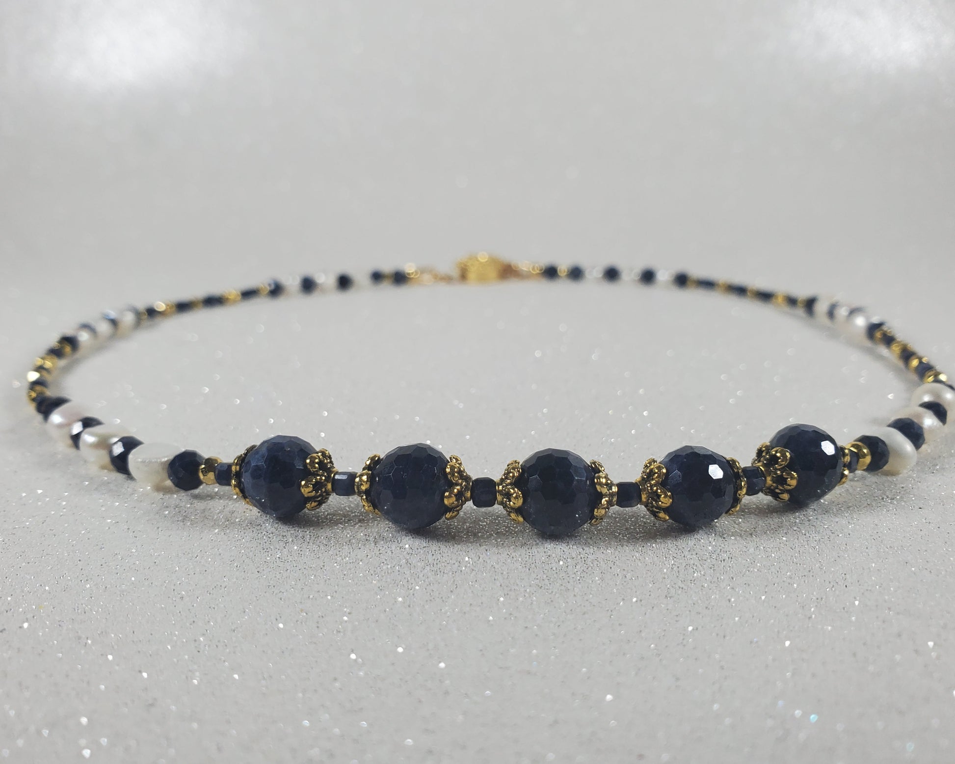 Navy blue beaded necklace with gold accents on a light gray background