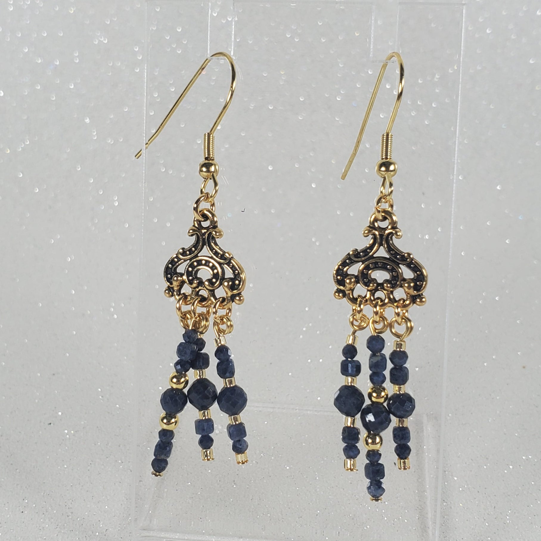 Pair of gold and blue beaded earrings on a clear card with a white background