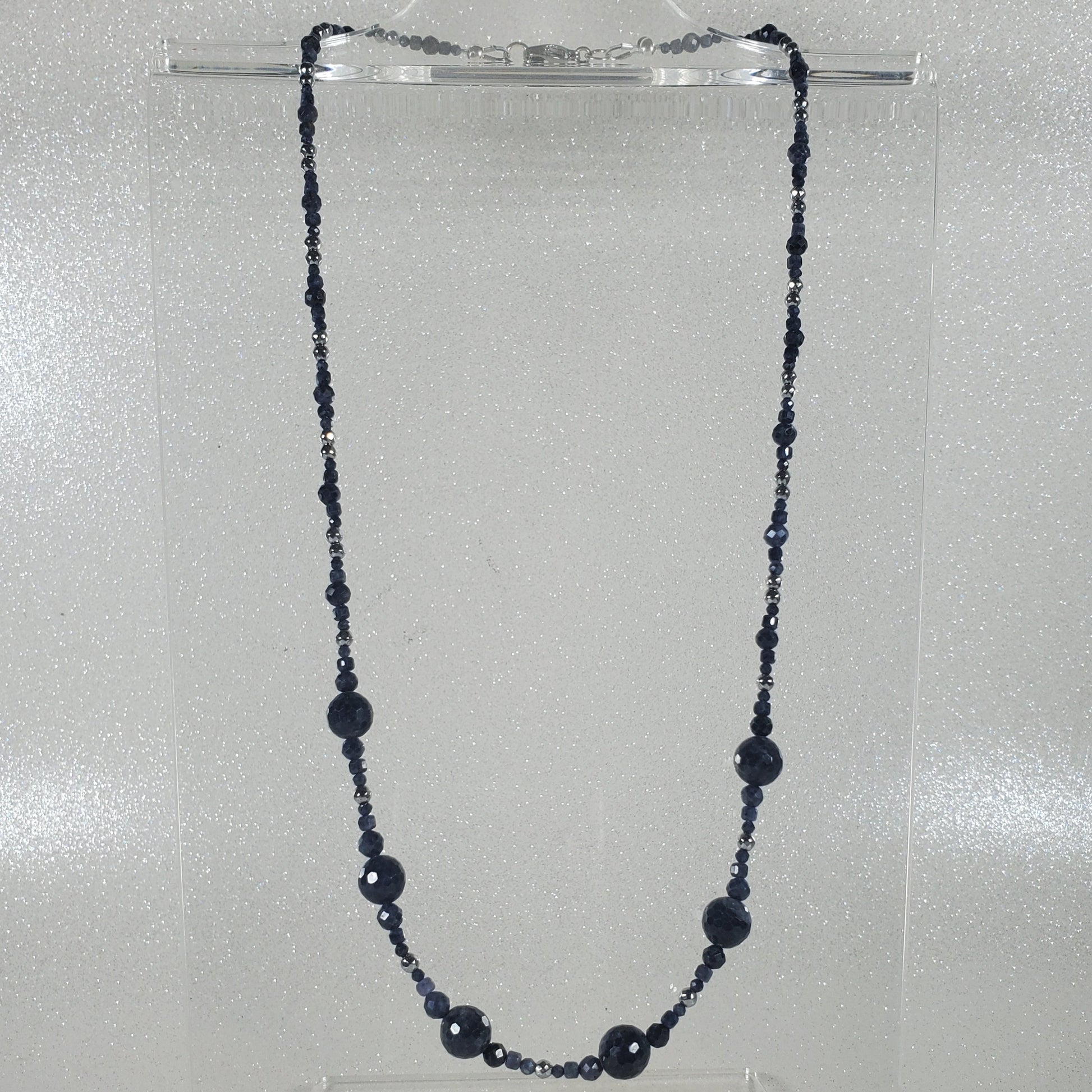 Blue beaded necklace on a clear stand against a gray background