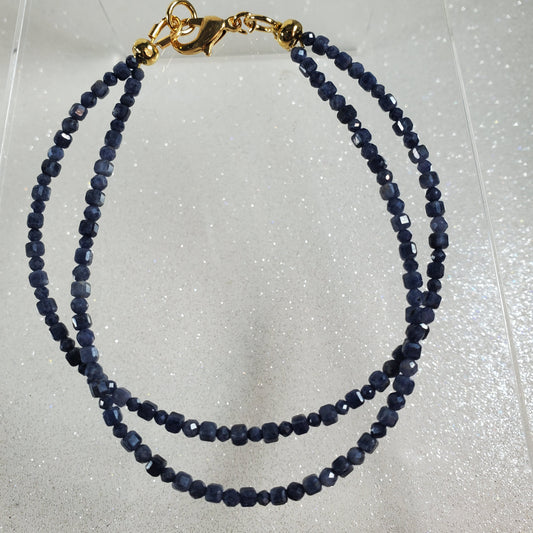Navy blue beaded necklace with a gold clasp on a light gray background
