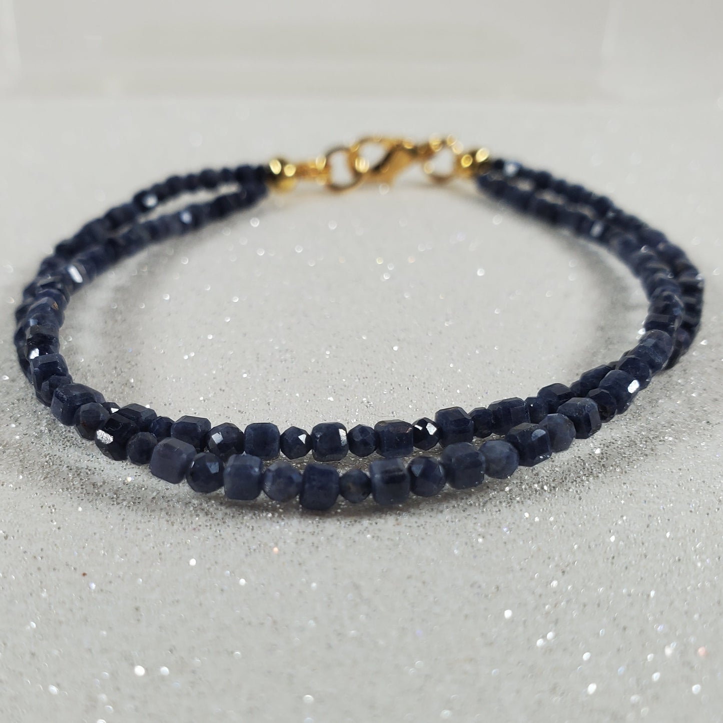 Navy blue beaded bracelet with a gold clasp on a glittery white background