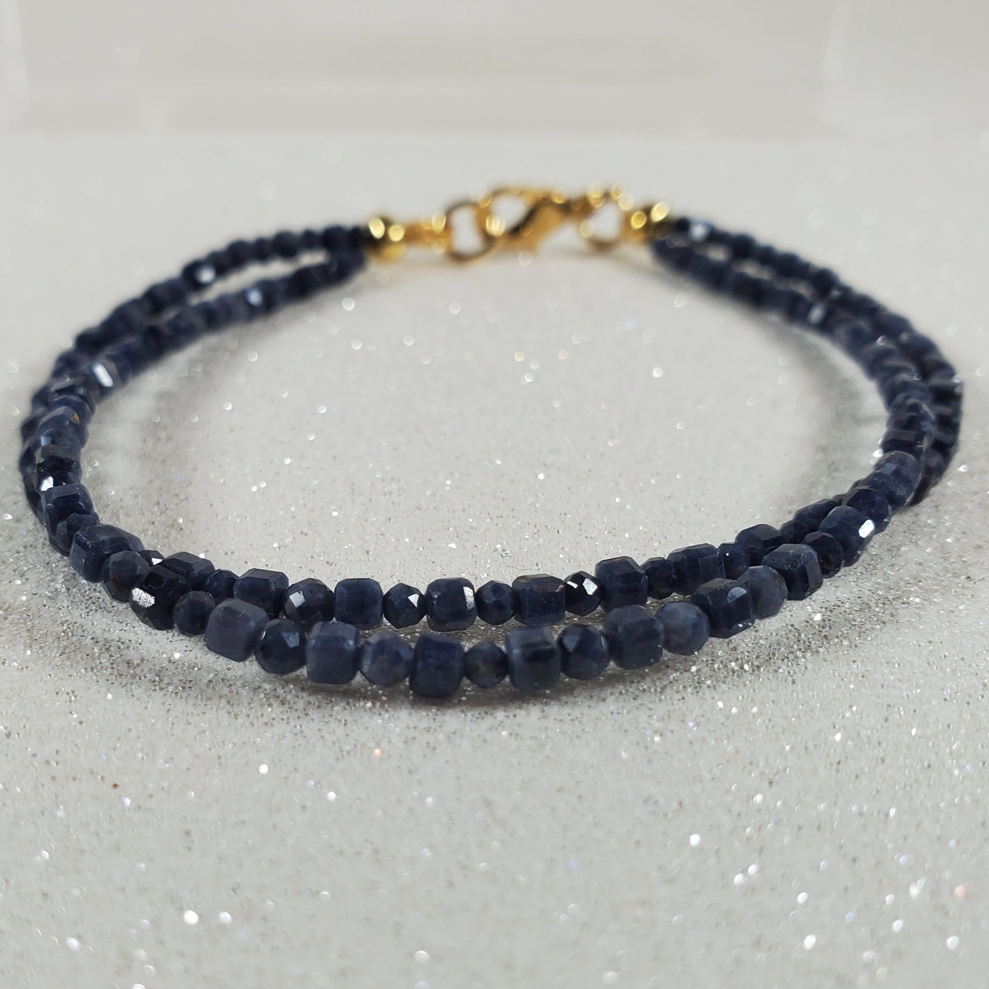 Navy blue beaded bracelet with a gold clasp on a glittery white background