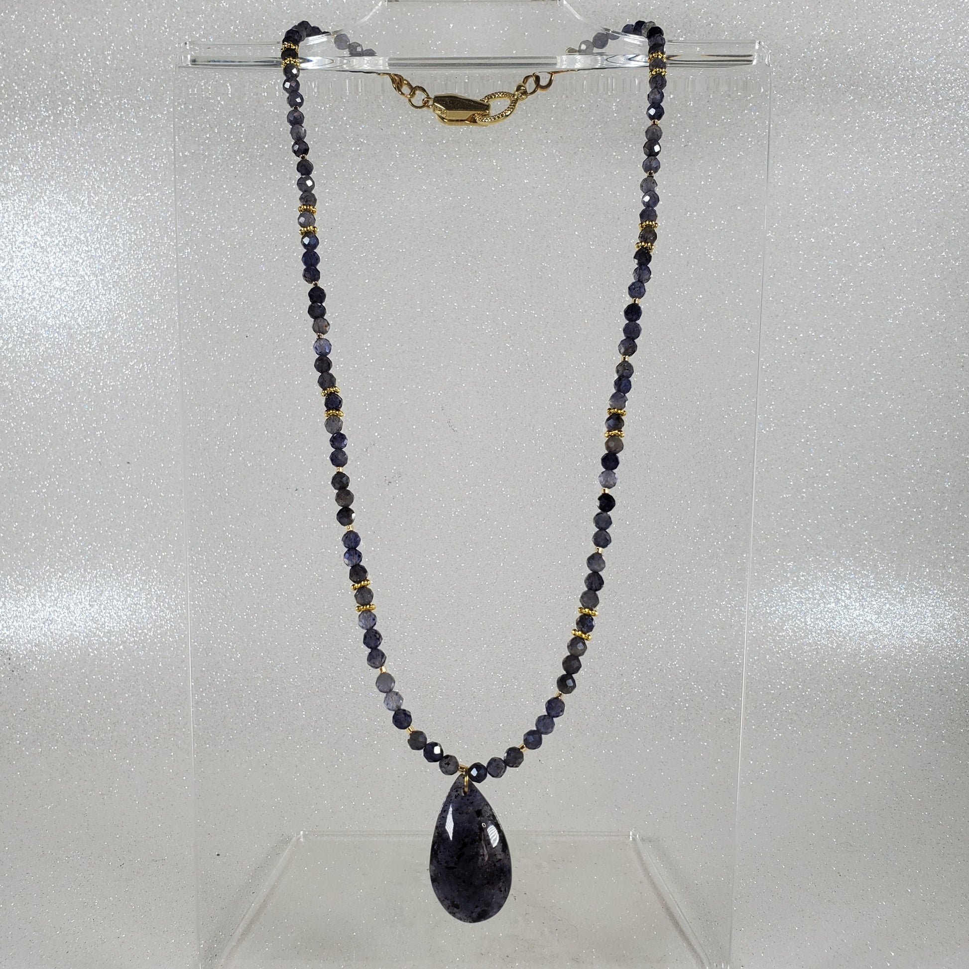Necklace with beads and a teardrop-shaped pendant on a clear stand against a light gray background