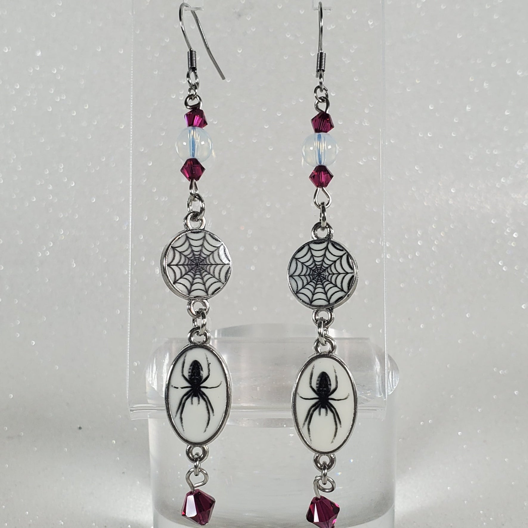 Two decorative earrings on a clear plastic stand against a white background
