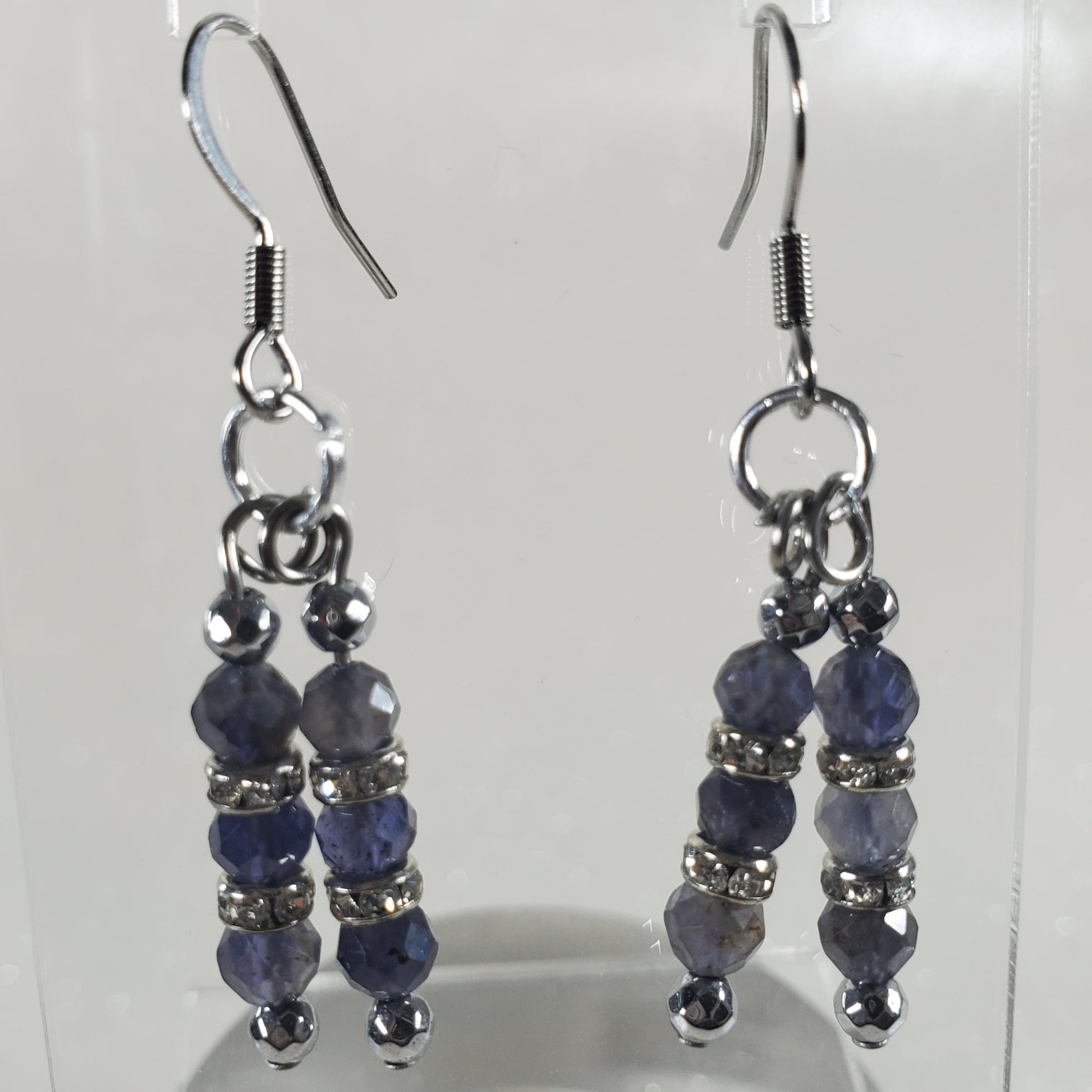 Pair of blue beaded earrings on a clear stand against a white background