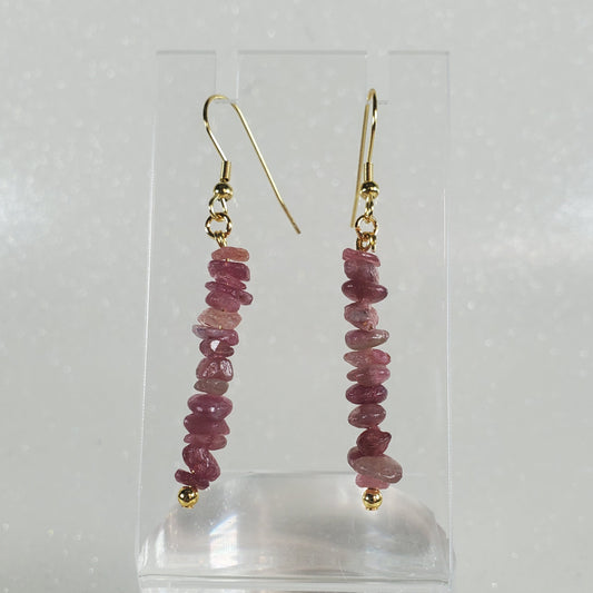 Pair of earrings with pink gemstones on a clear stand against a white background