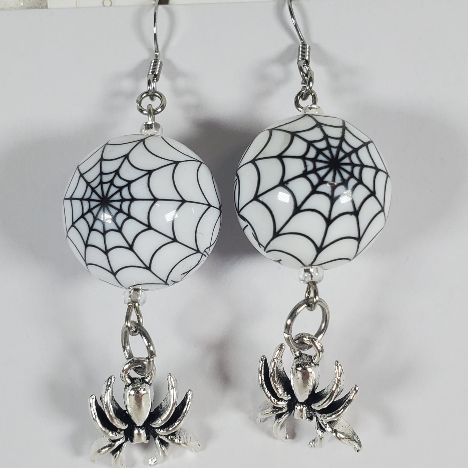 Spider web and spider earrings on a white card with a gray background
