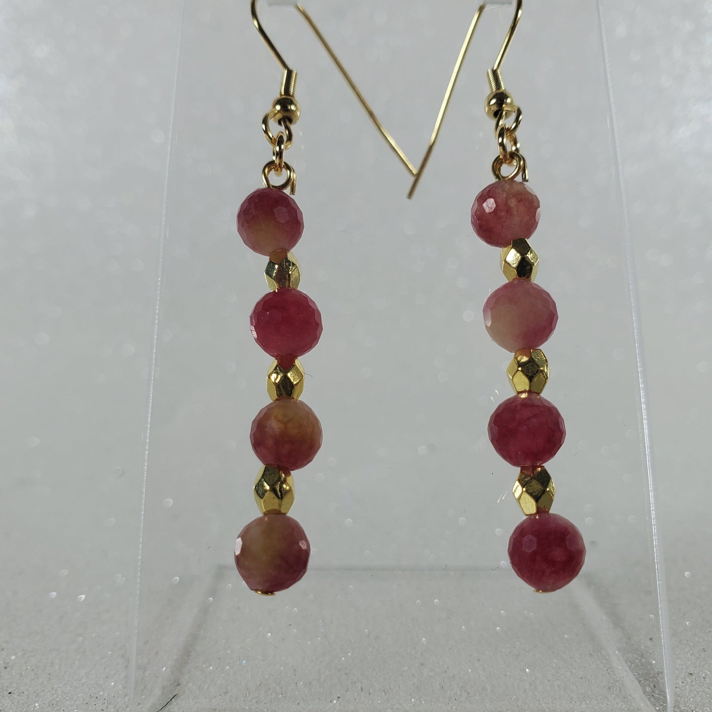 Pair of earrings with red beads and gold accents on a clear stand against a white background