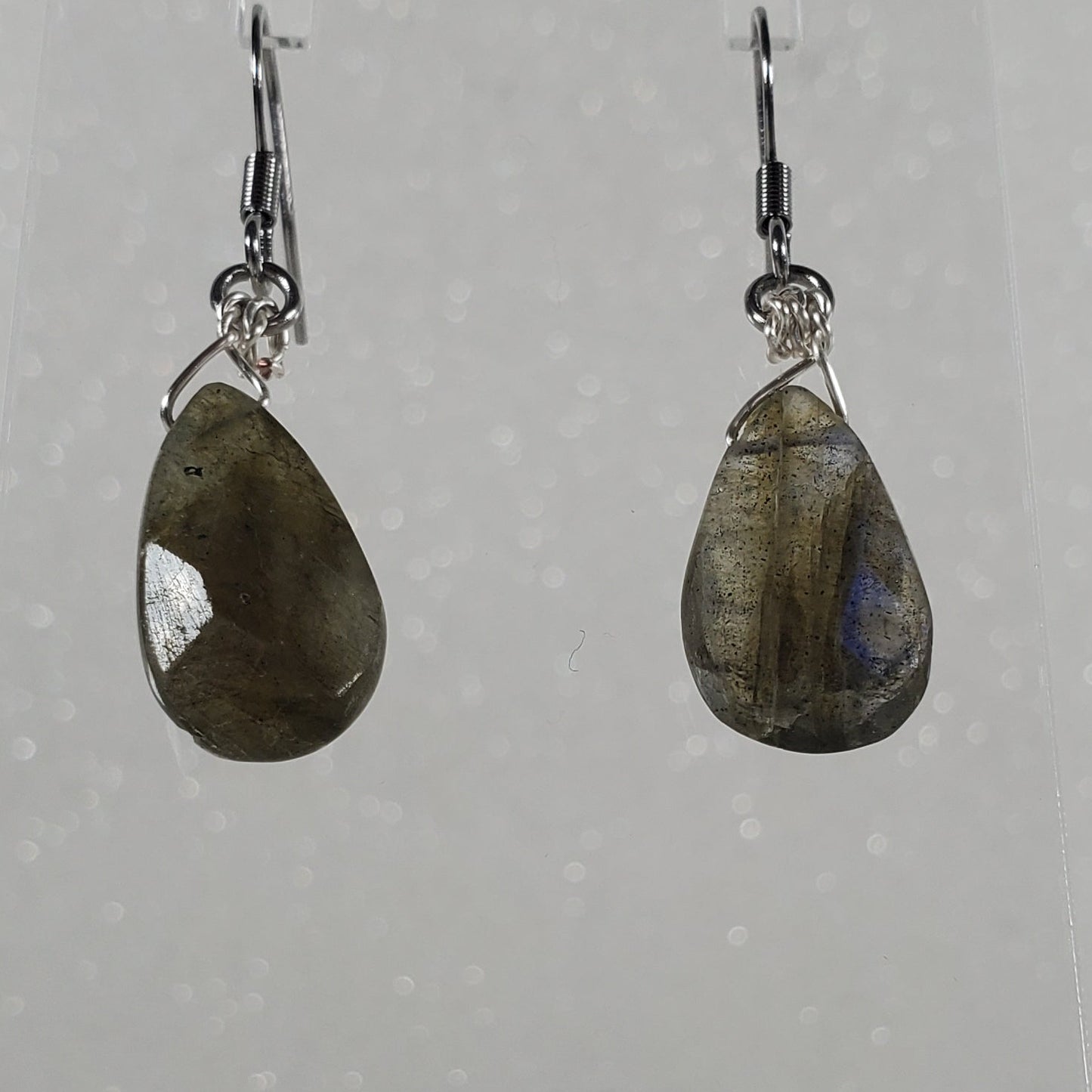 Teardrop-shaped earrings on a clear stand against a white background