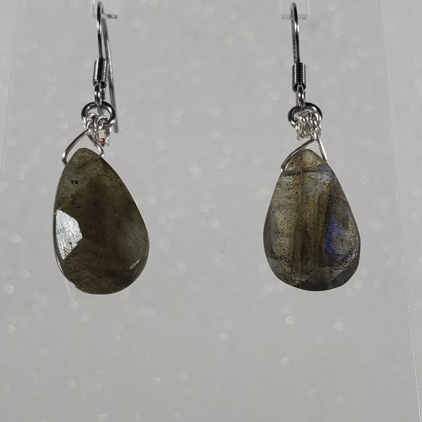 Teardrop-shaped earrings on a clear stand against a white background