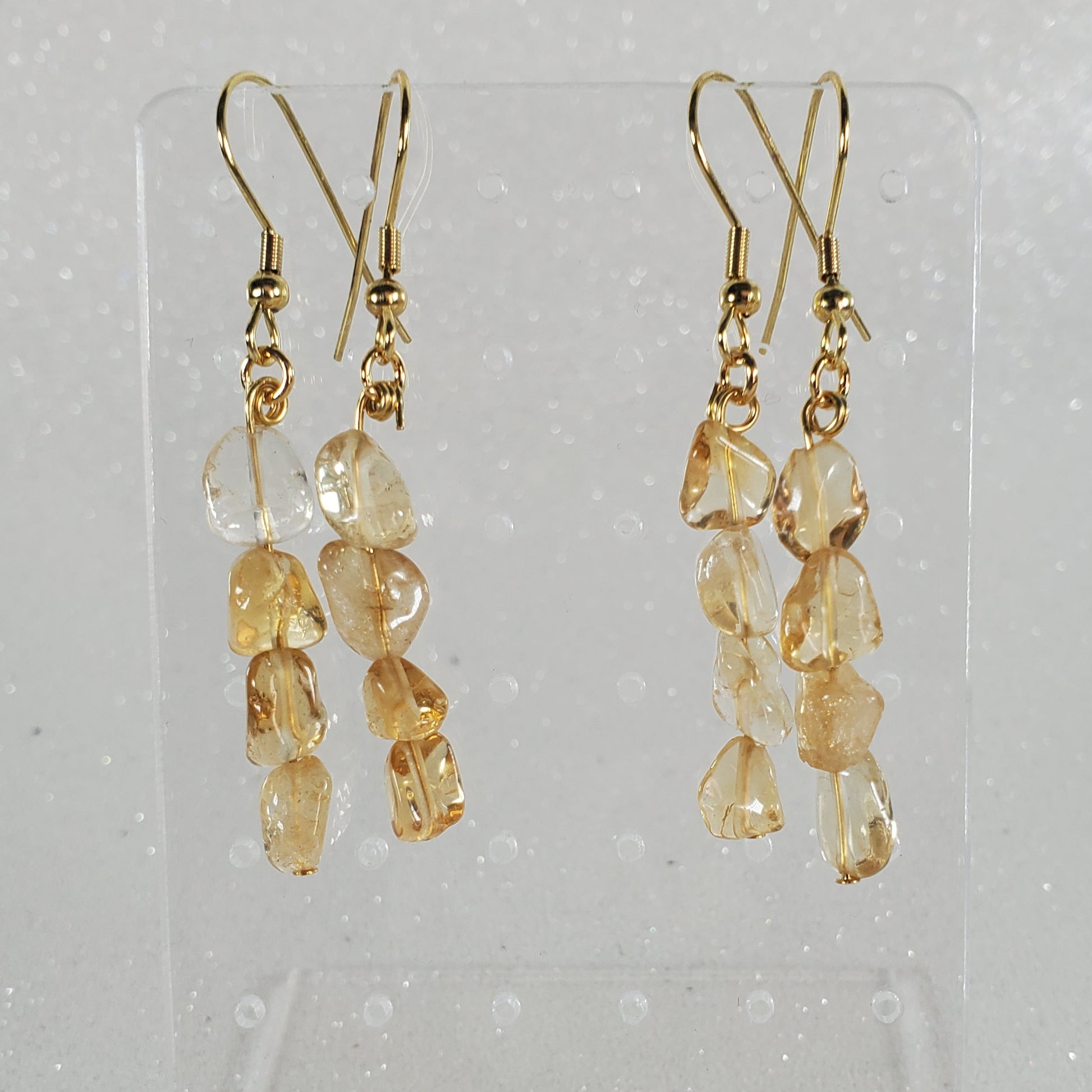 Pair of gold and beige beaded earrings on a clear stand against a light gray background