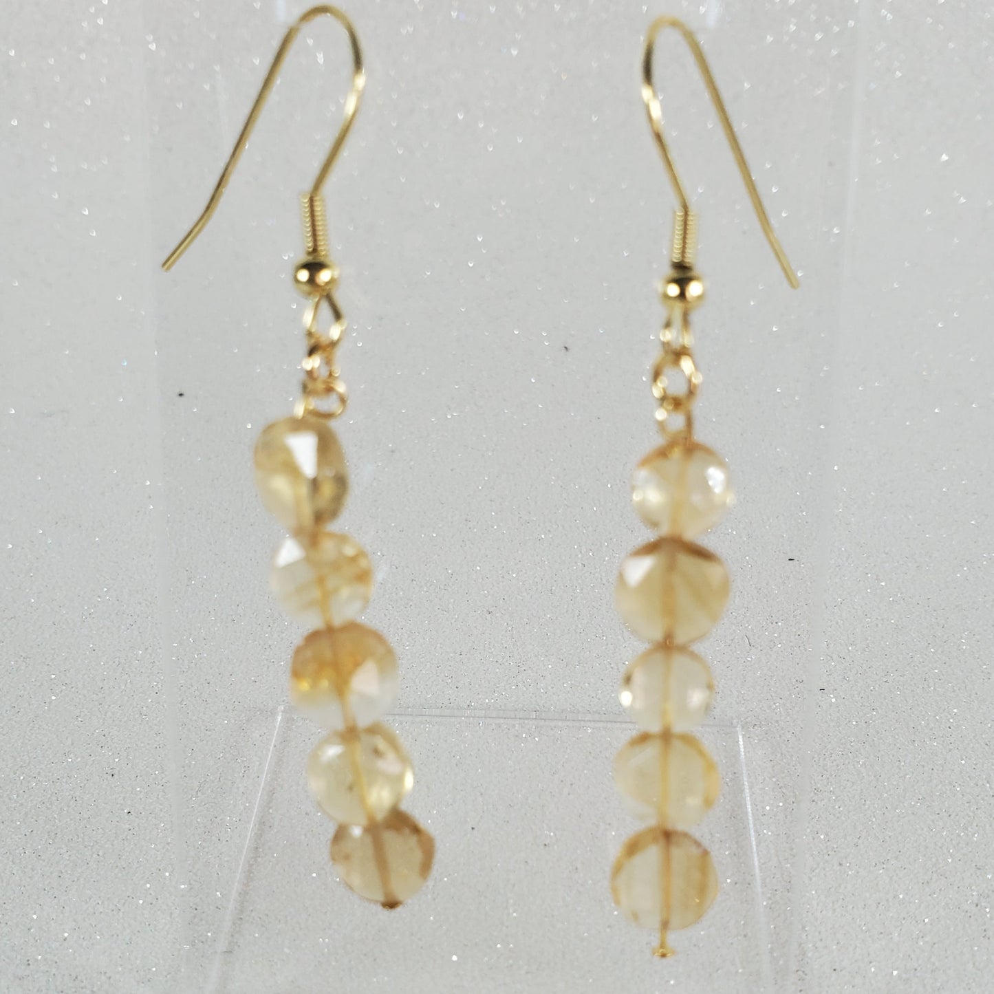 Gold earrings with clear beads on a light gray background