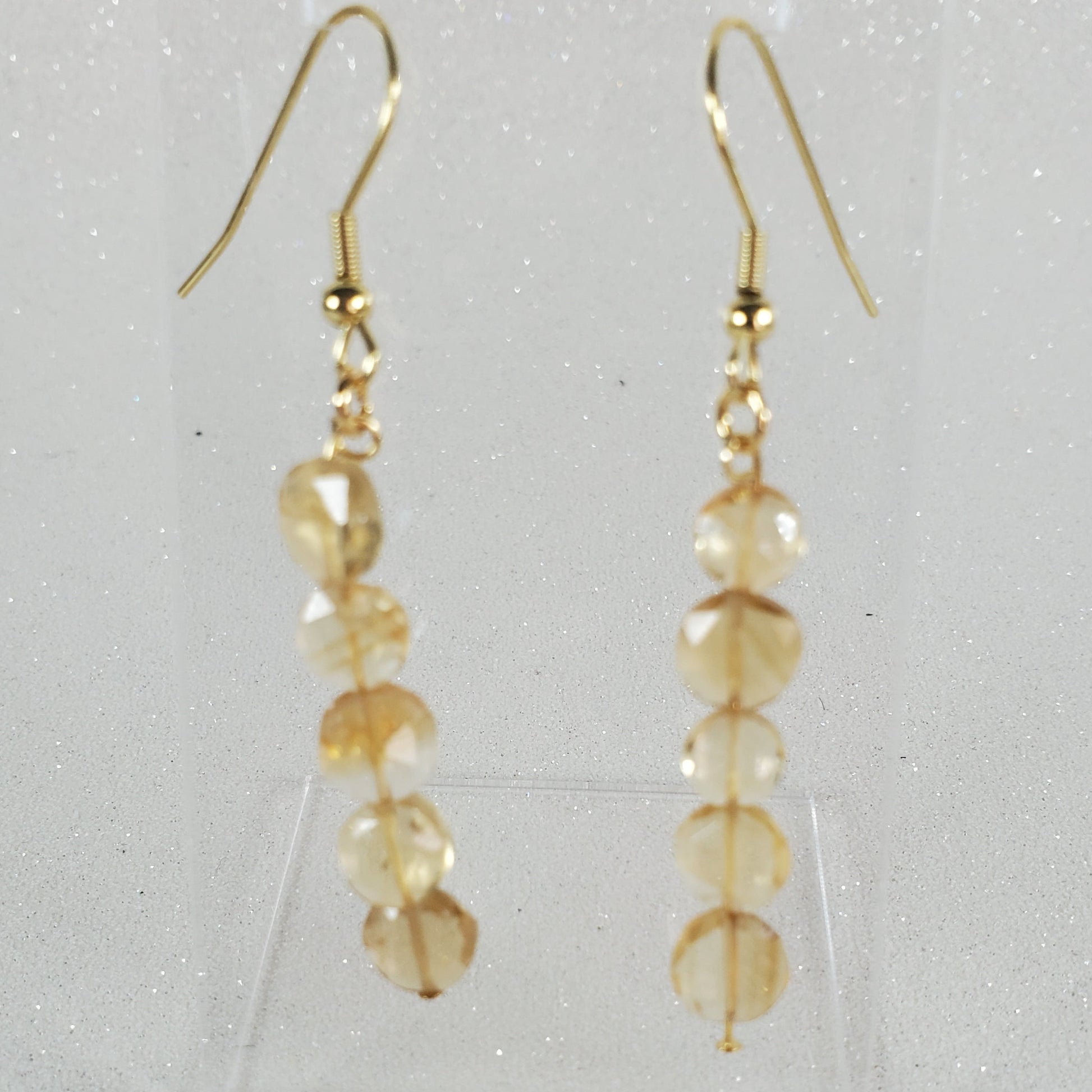 Gold earrings with clear beads on a light gray background
