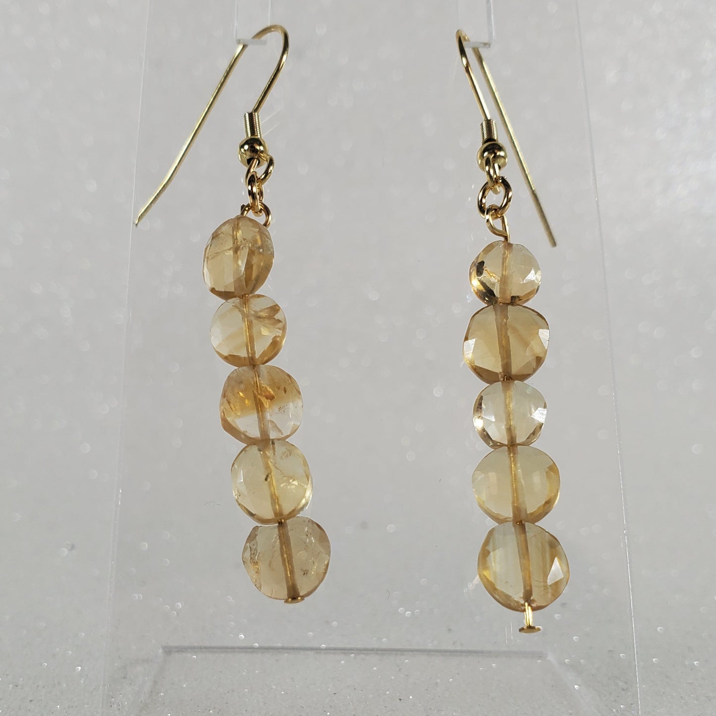 Pair of gold earrings with circular beads on a clear stand against a light gray background