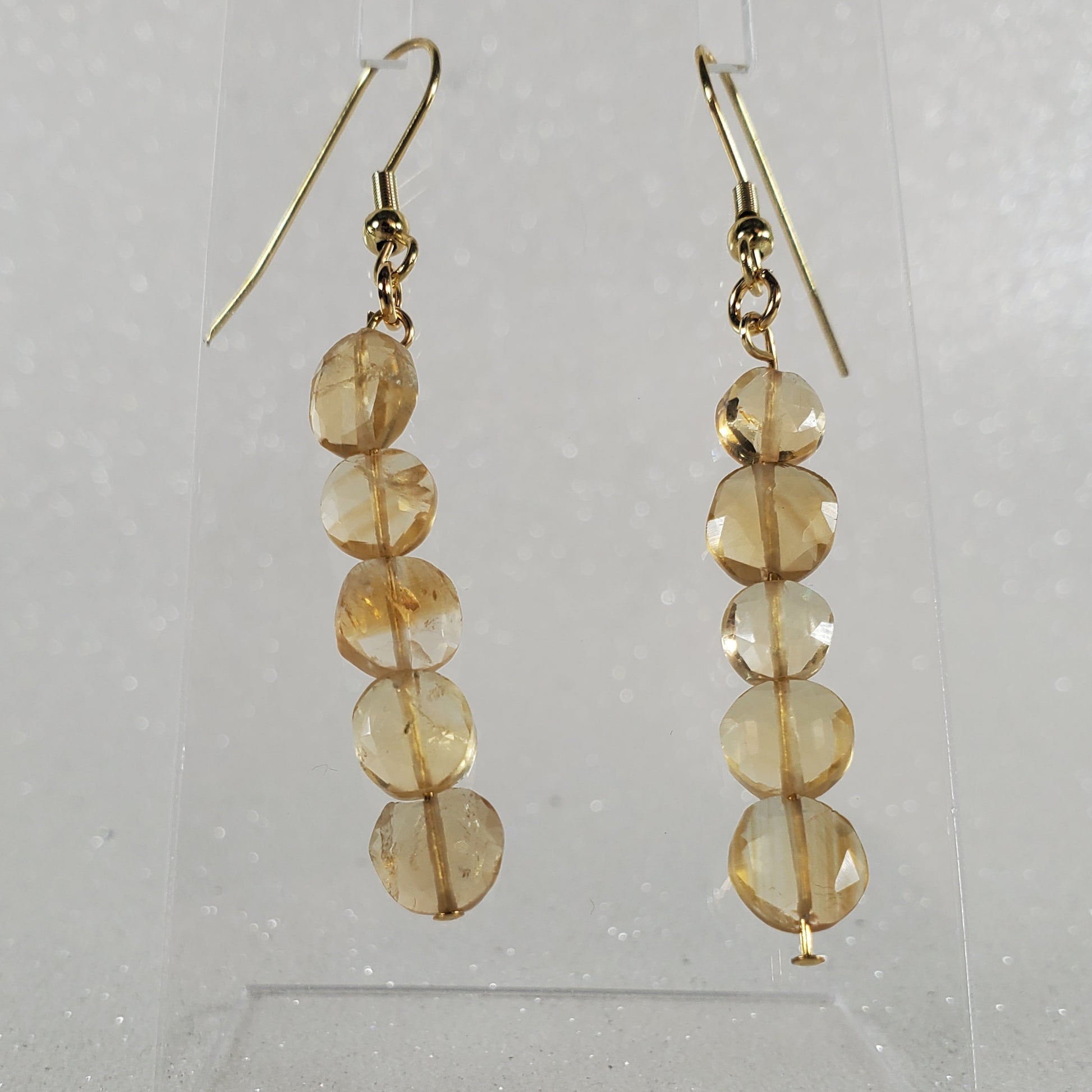 Pair of gold earrings with circular beads on a clear stand against a light gray background
