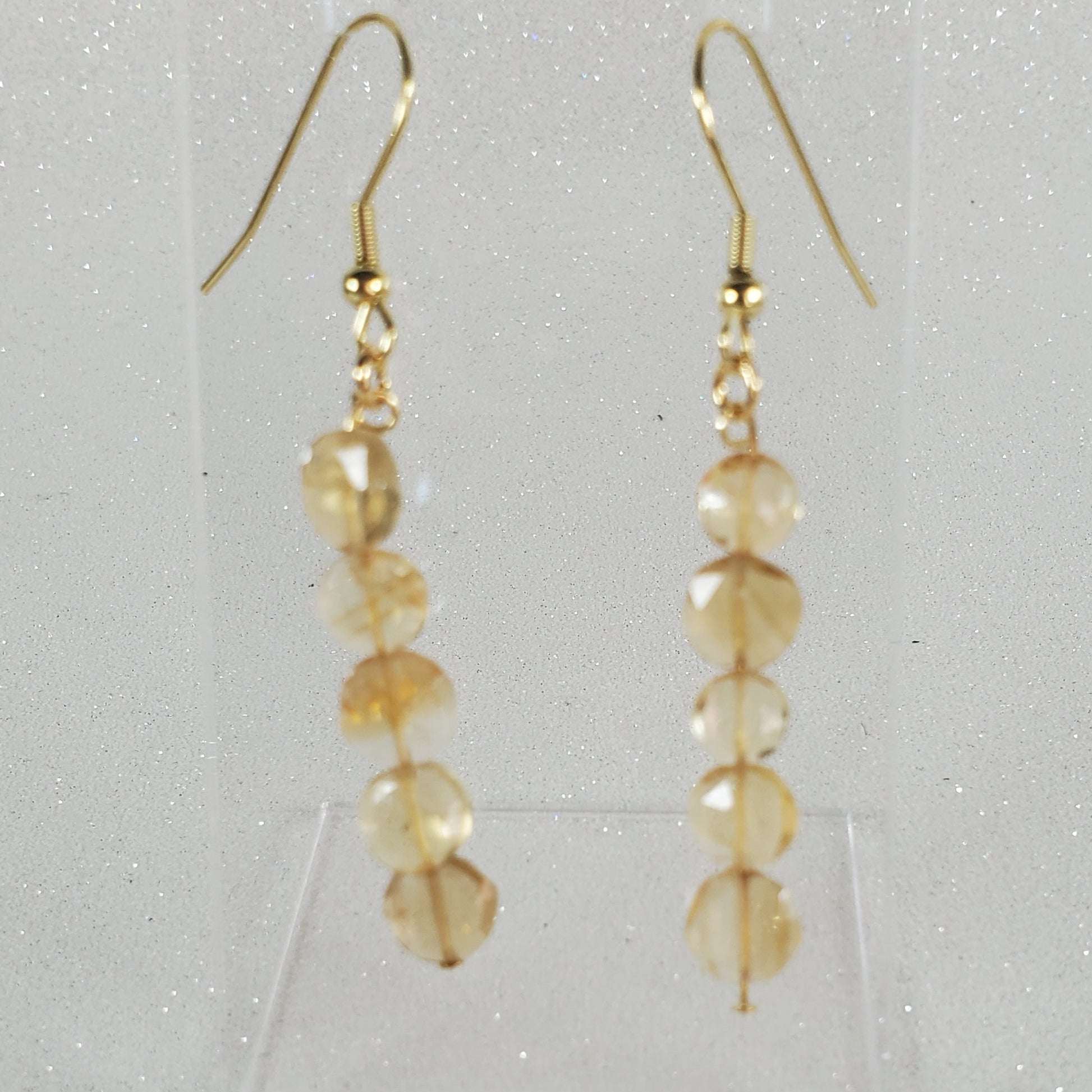 Gold beaded earrings on a clear stand against a light gray background
