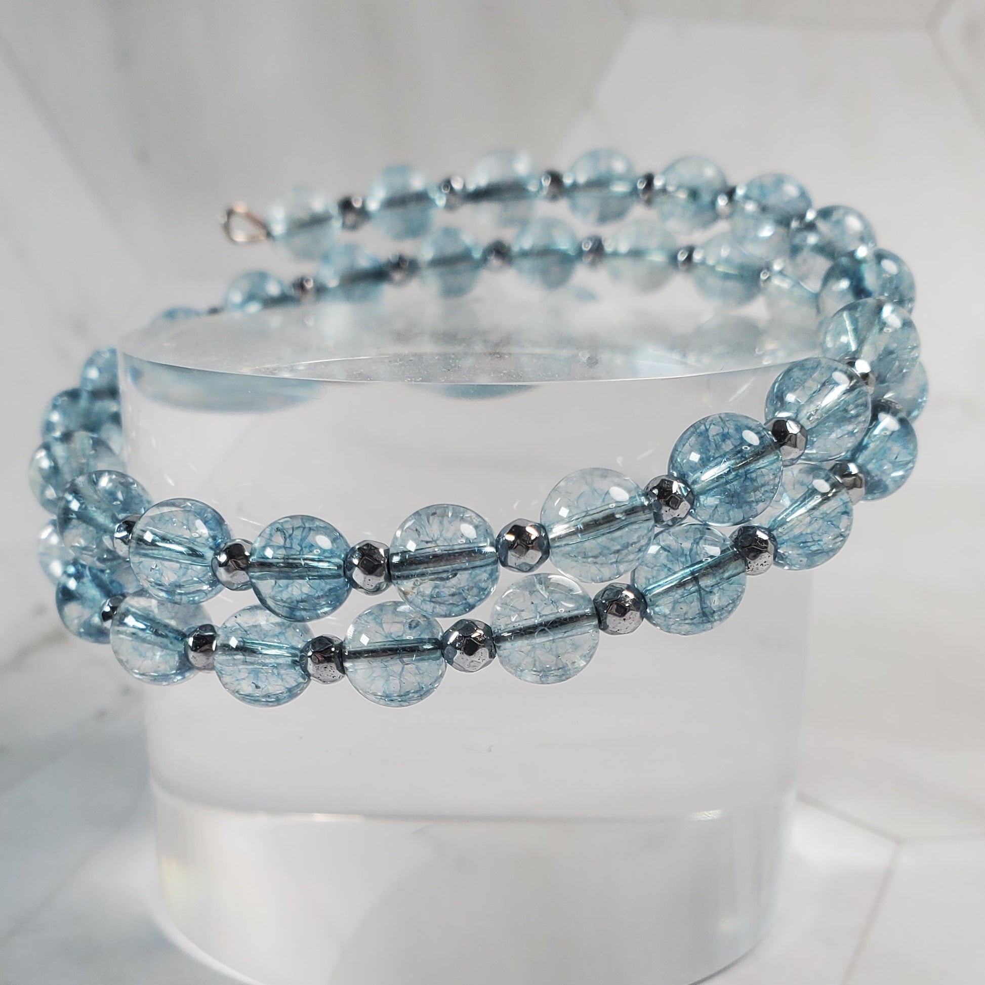 Blue beaded bracelet on a white pedestal against a marble background