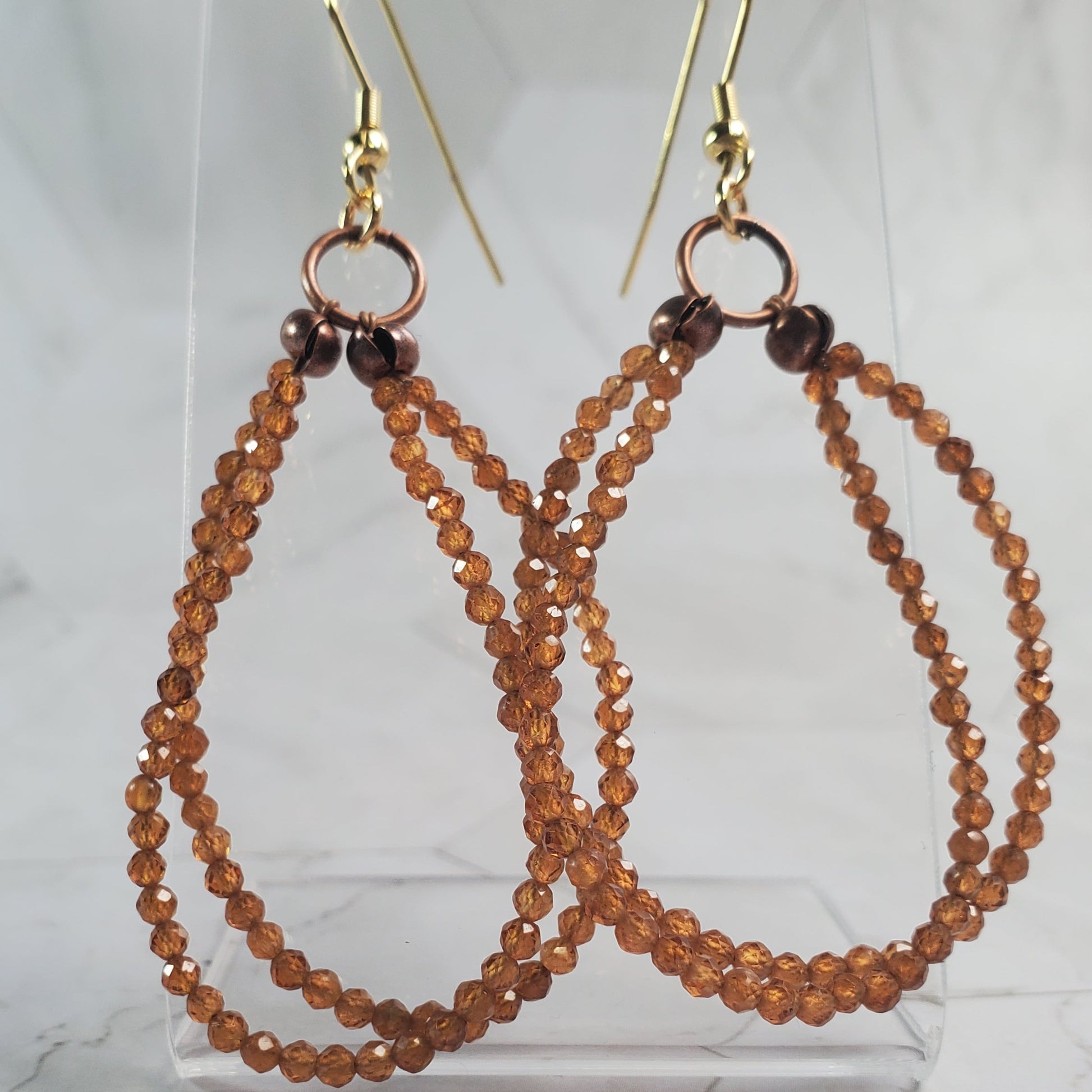 Pair of beaded earrings on a clear stand against a marble background