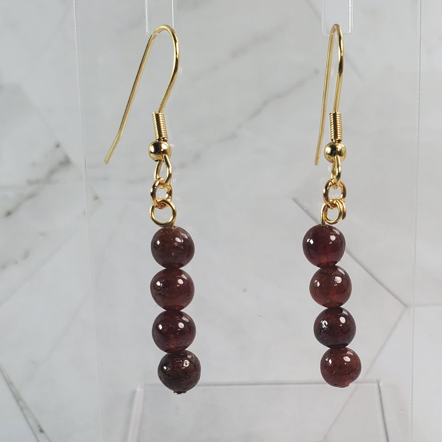 Pair of gold earrings with red beads on a marble surface