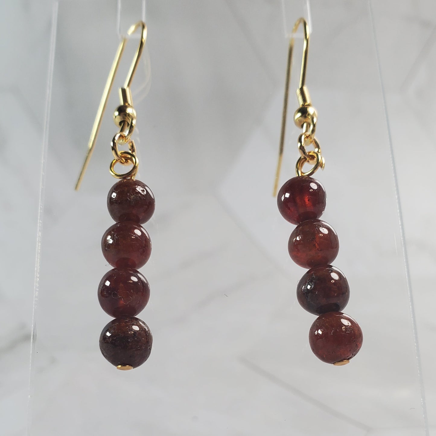 Garnet bead earrings on gold hooks against a marble background