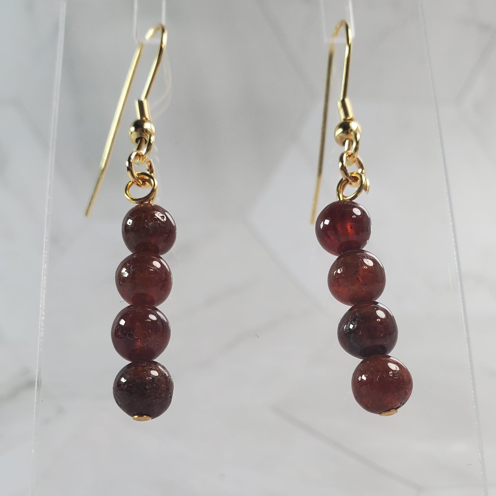 Garnet bead earrings on gold hooks against a marble background