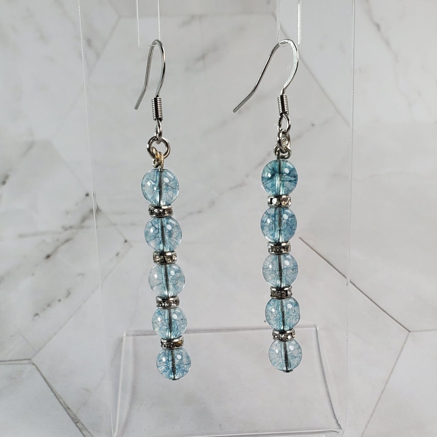 Pair of beaded earrings on a clear stand against a marble background