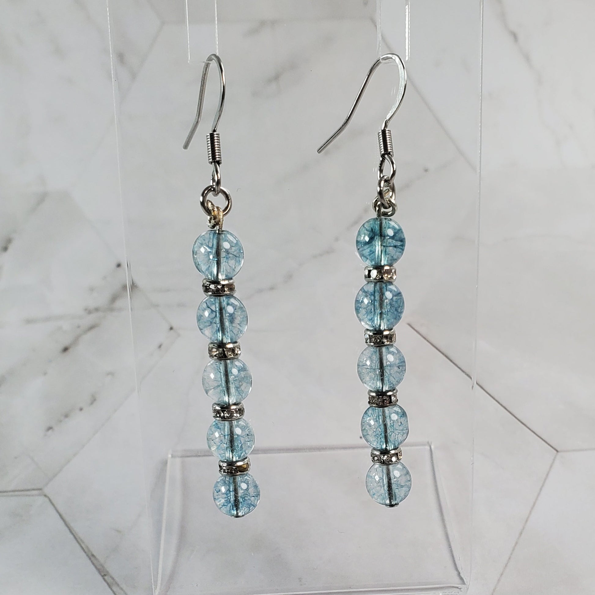 Pair of beaded earrings on a clear stand against a marble background